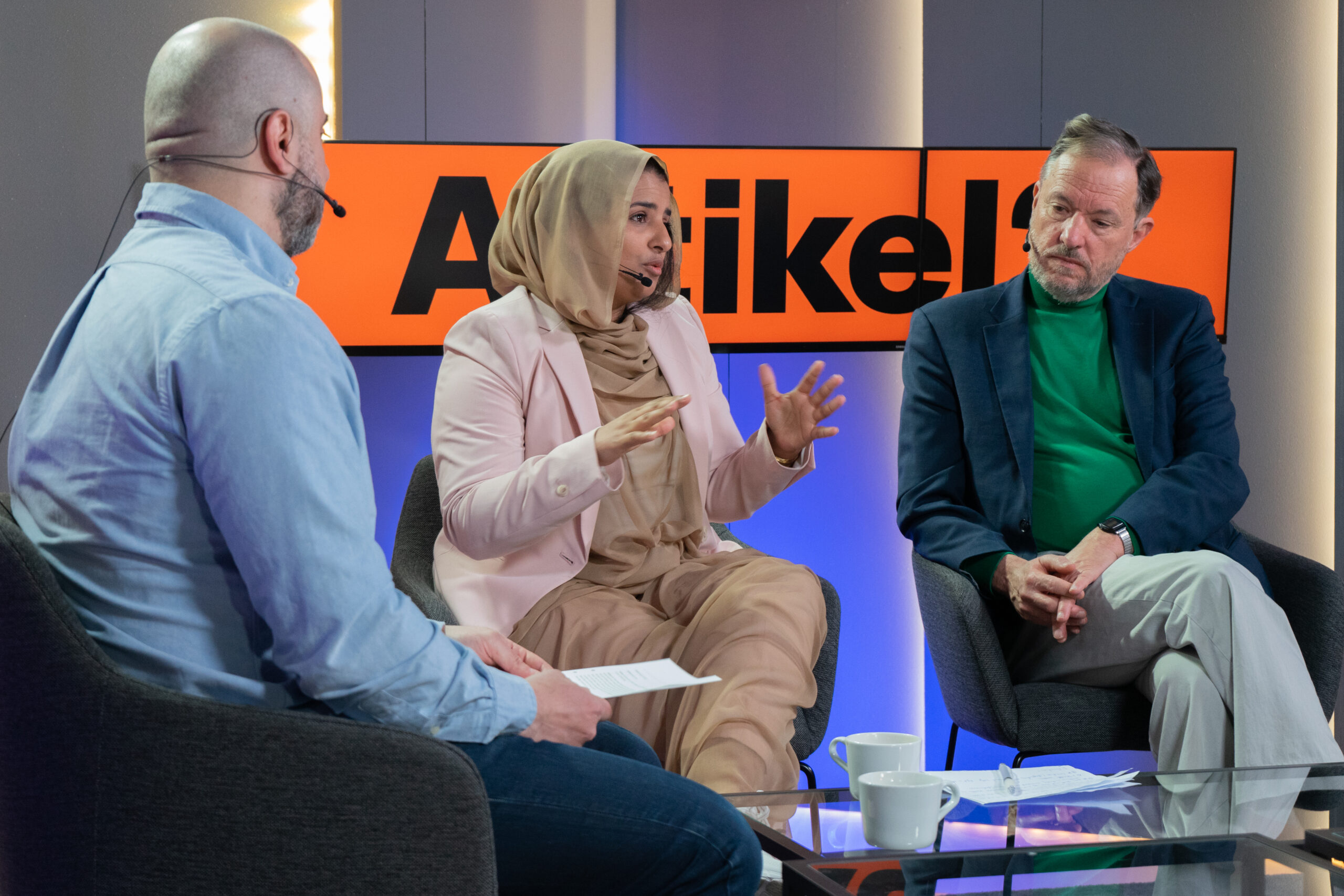 Tre personer deltar i en paneldiskussion, där kvinnan i mitten gestikulerar medan hon talar.