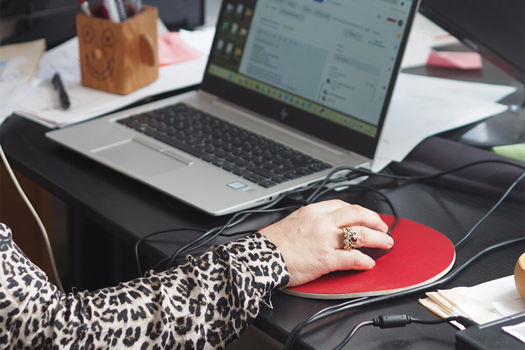 En hand som styr en datormus på en kontorsplats med en dator.