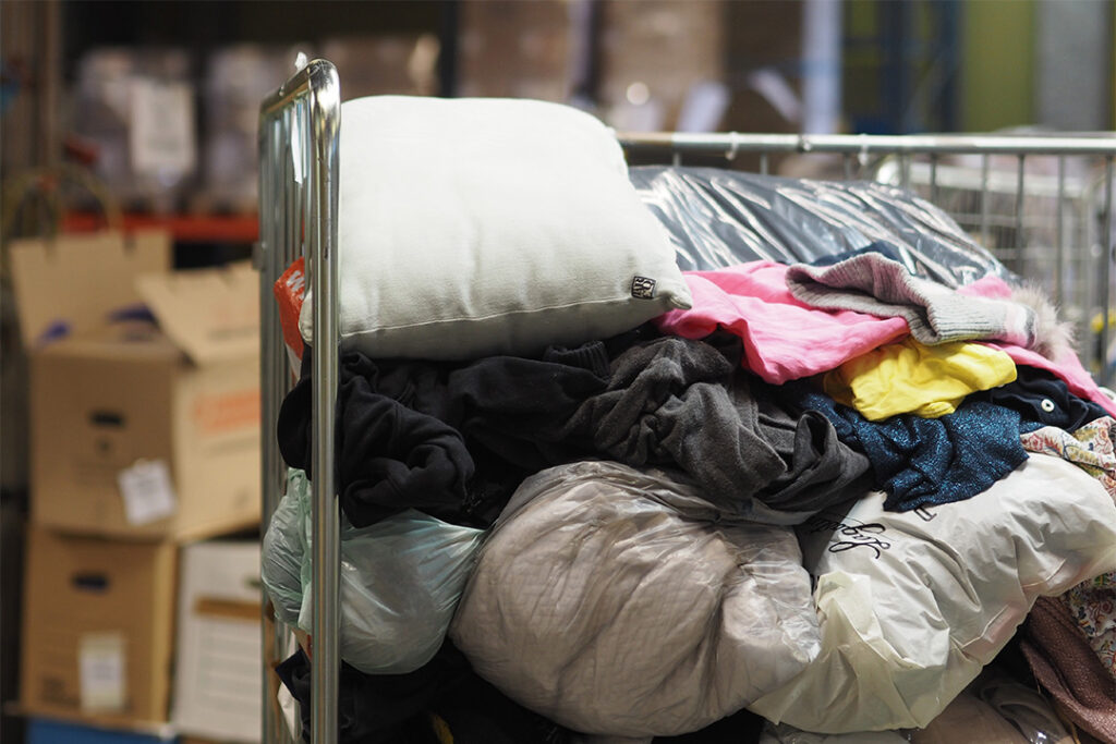Rullbinge med kläder i. I bakgrunden skymtar ännu mer kläder och kartonger.