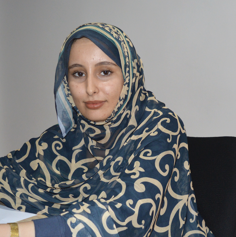 Asma_50kampanj Asma sitter på ett kontor. Hon har en melfa på sig och tittar in i kameran.