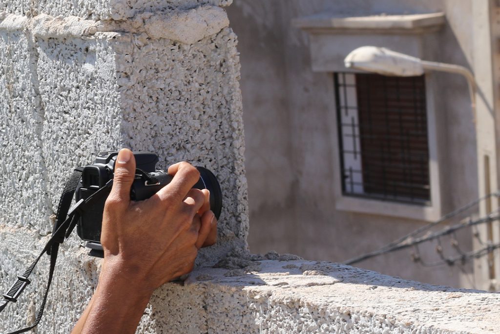 En hand som håller i en kamera och fotar genom en öppning i en mur.