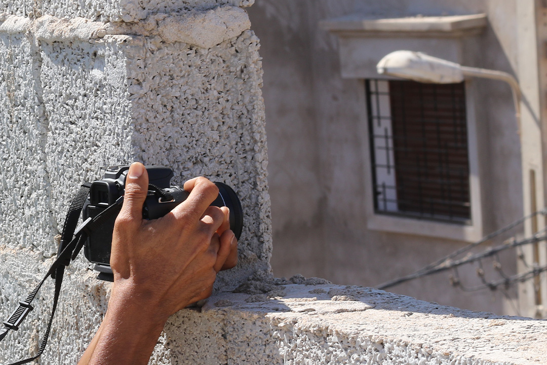 En hand som håller i en kamera och fotar genom en öppning i en mur.